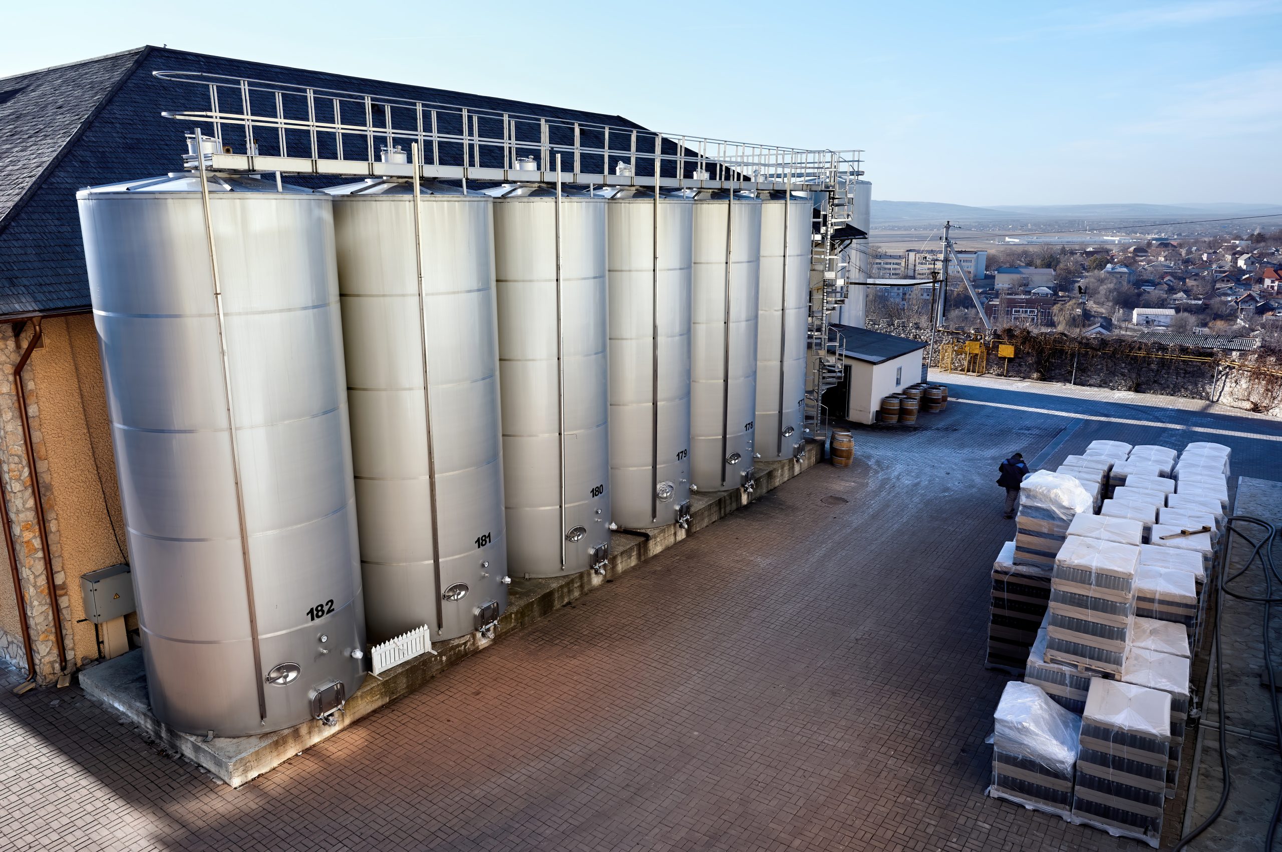 Metal wine storage tanks with dwelling houses on the background in a winery Metal wine storage tanks with dwelling houses on the background in a winery. Wide shot