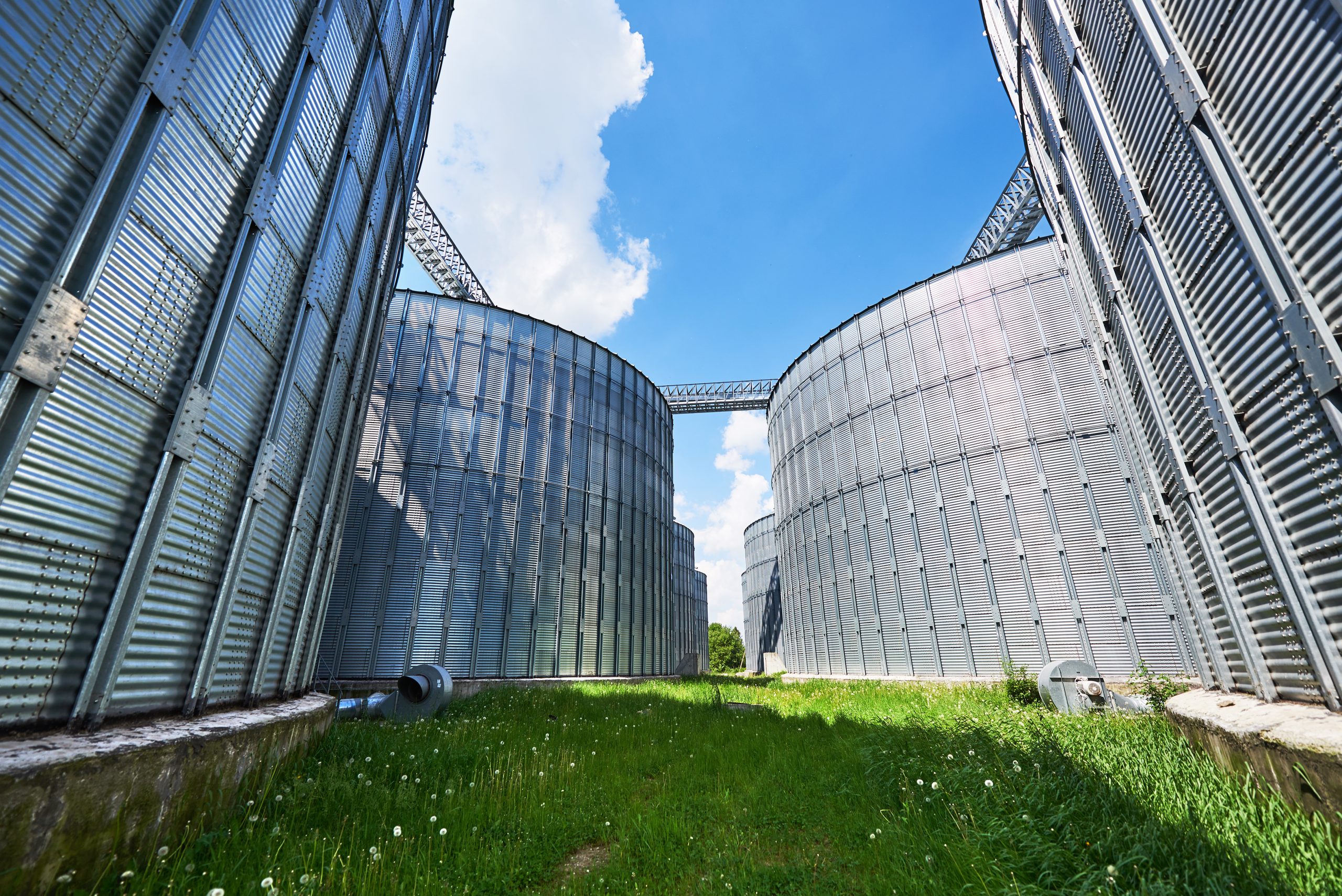 Agricultural Silos. Building Exterior. Storage and drying of grains, wheat, corn, soy, sunflower against the blue sky with white clouds Agricultural Silos. Building Exterior. Storage and drying of grains, wheat, corn, soy, sunflower against the blue sky with white clouds.